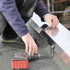 Ein Klempner der auf einem Flachdach arbeitet mit einem Akkubohrer