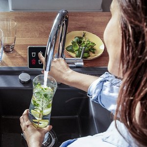 Erfrischendes Getränk mit Zitrone und Minze zubereiten Eine Person füllt ein Glas mit Wasser, das frische Minze und Zitronenscheiben enthält, aus einem modernen Wasserhahn.
