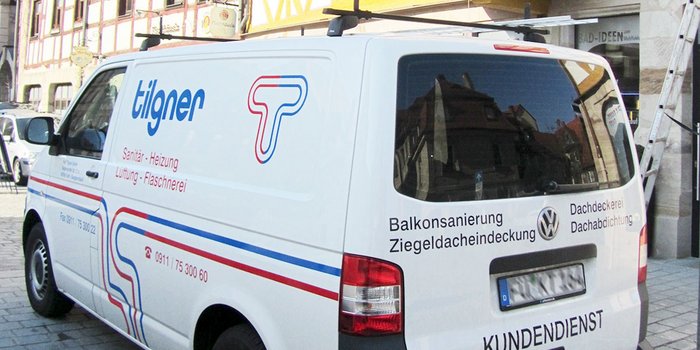 Der Lieferwagen von 'Tilgner' ist mit Informationen zu Dach- und Sanitärdiensten beschriftet und parkt vor einem historischen Gebäude.