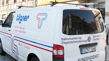 Fahrzeug des Sanitär- und Heizungsdienstes in der Stadt Der Lieferwagen von 'Tilgner' ist mit Informationen zu Dach- und Sanitärdiensten beschriftet und parkt vor einem historischen Gebäude.